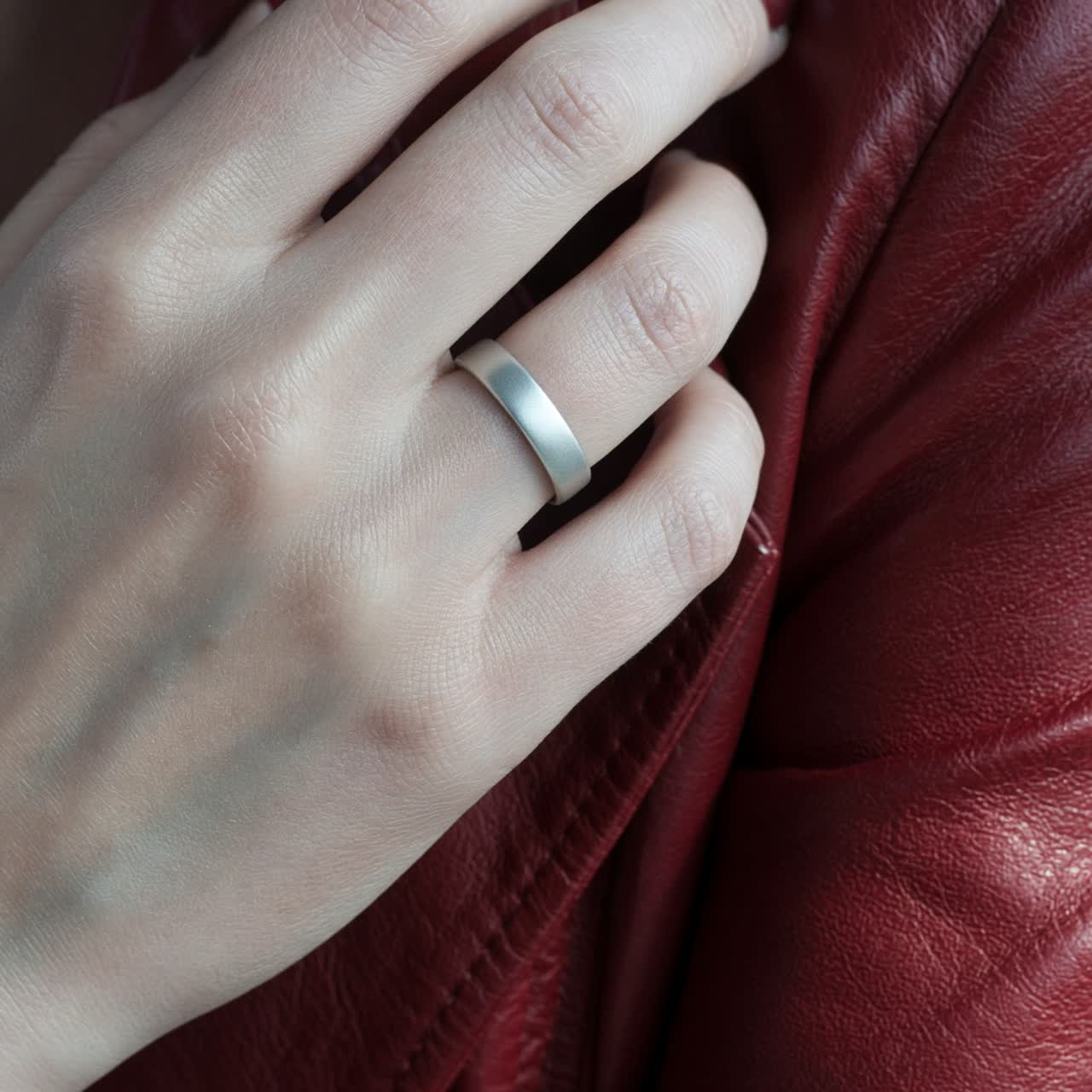 Close view of a silver smart ring on a hand against a red leather jacket
